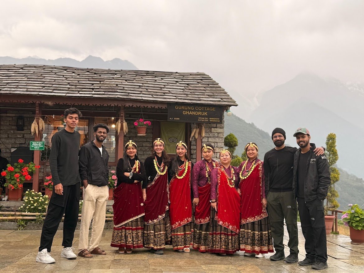 Tourists with local women in traditional Gurung dress at Gurung Cottage Ghandruk Nepal, showcasing cultural hospitality and mountain views.