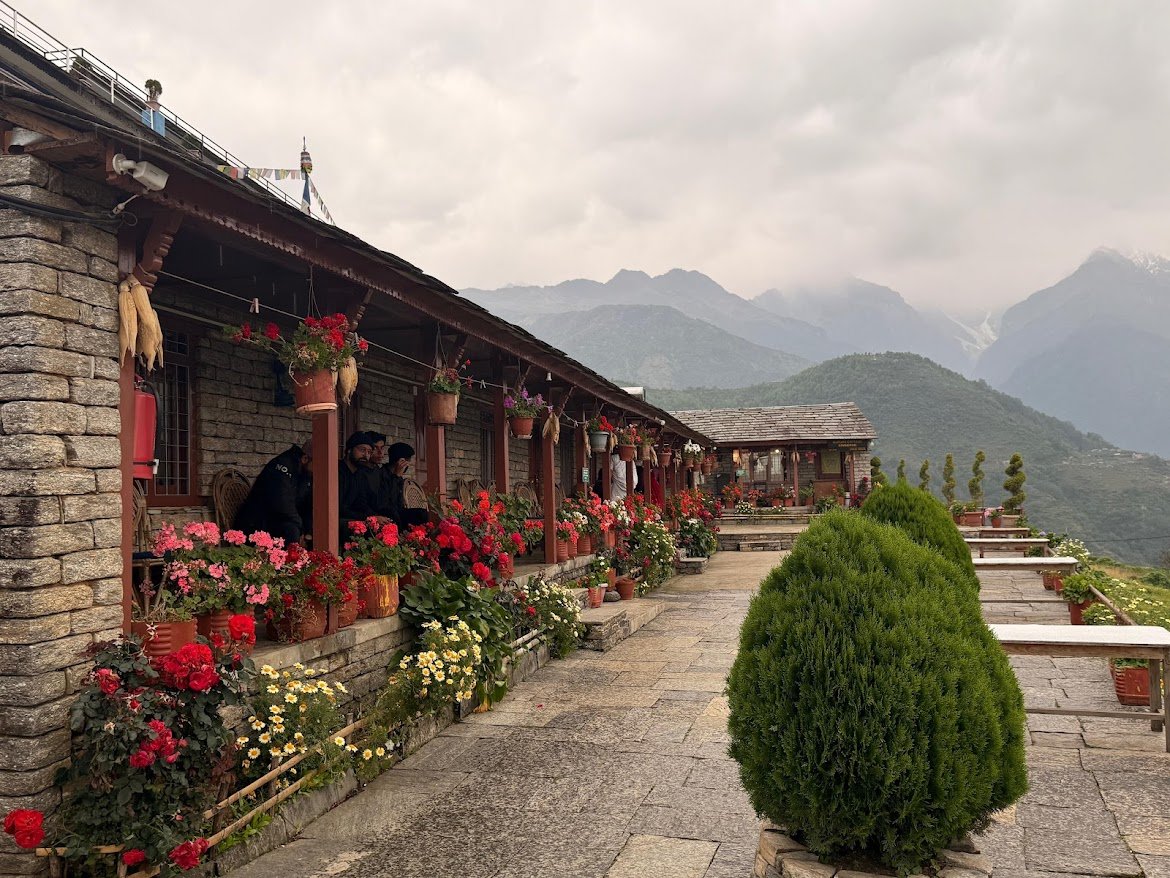 raditional Gurung stone cottage in Ghandruk, Nepal, surrounded by vibrant flowers and misty Himalayan mountains on a rainy morning.