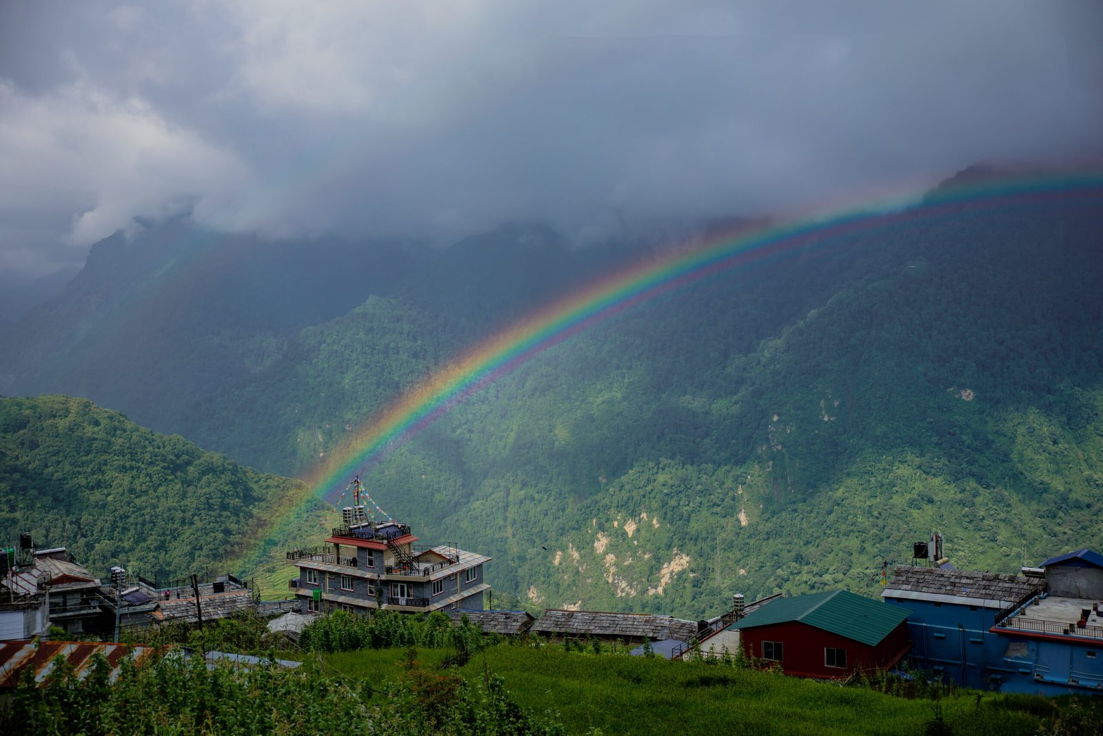 Rainbow over Ghandruk village during monsoon season, showcasing lush greenery and mountain village charm in Nepal.