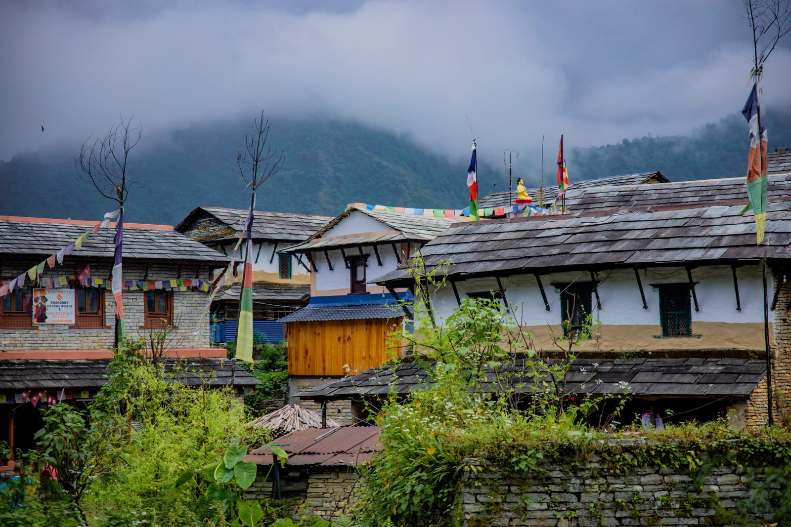 Stone-roofed traditional Gurung houses in Ghandruk village, Nepal, with prayer flags and misty mountains in the background, photographed by Subash Thapa Magar.